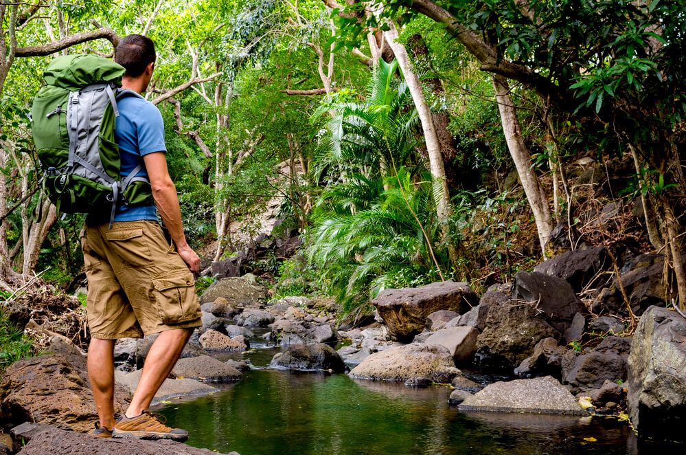 Image of a male hiker with a green backpack standing near a river on Oahu