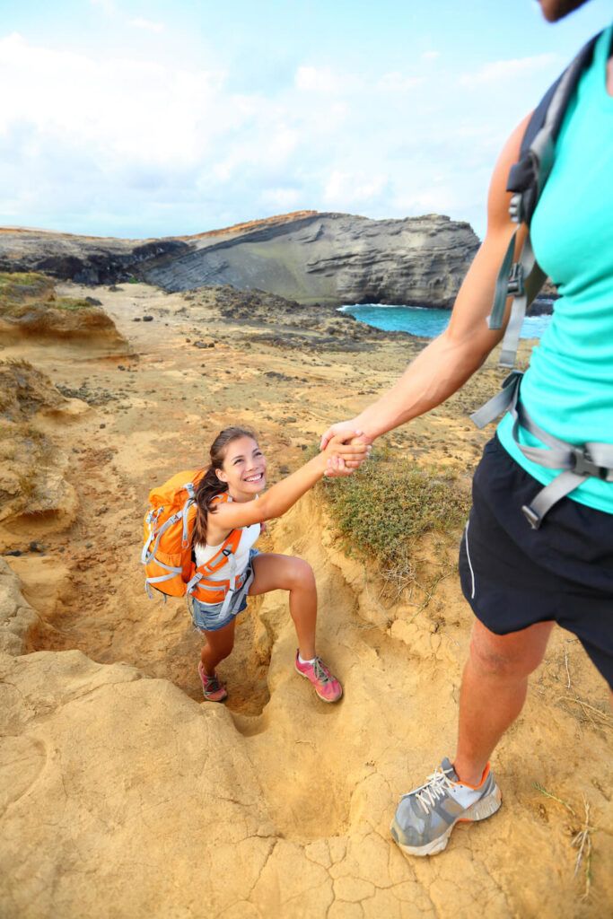 Image of a man hiker helping up a woman hiker as they hike on the Big Island of Hawaii