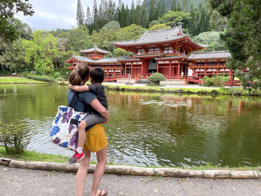 Image of a mom holding a boy as they look at a red temple with water in front