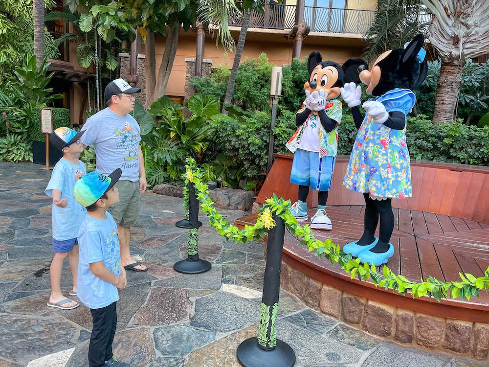 Image of a dad and two boys chatting with Mickey and Minnie who are dressed in Hawaiian clothing at Disney Aulani Resort