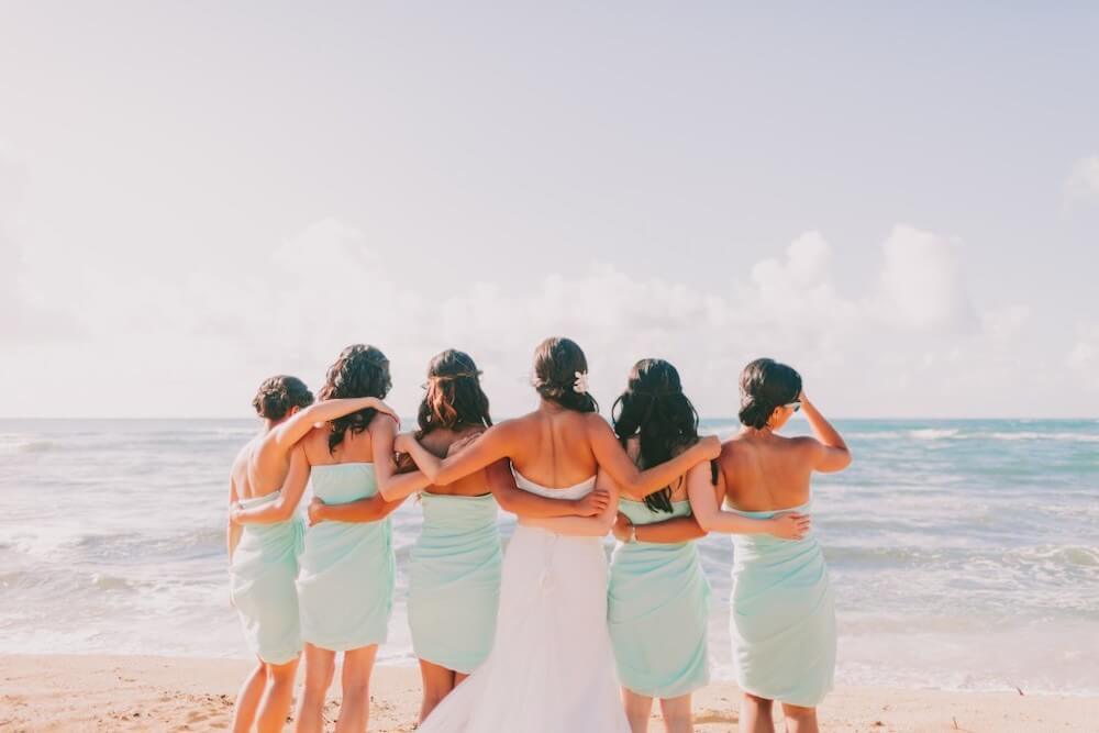 Image of a bride and 5 bridesmaids wearing light blue facing the ocean for a wedding in Hawaii.