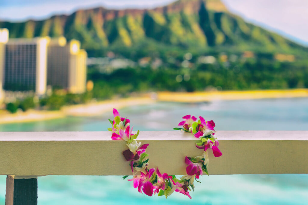 Image of a colorful lei draped over a railing in front of Waikiki Beach and Diamond Head.
