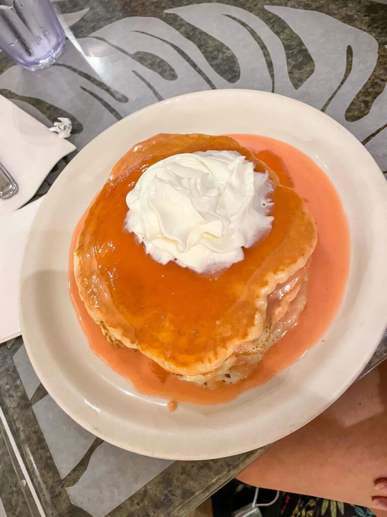 Image of a plate of pink pancakes with whipped cream on top