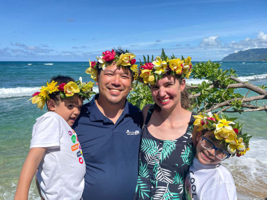 Image of a family wearing leis on their heads with the ocean in the background.