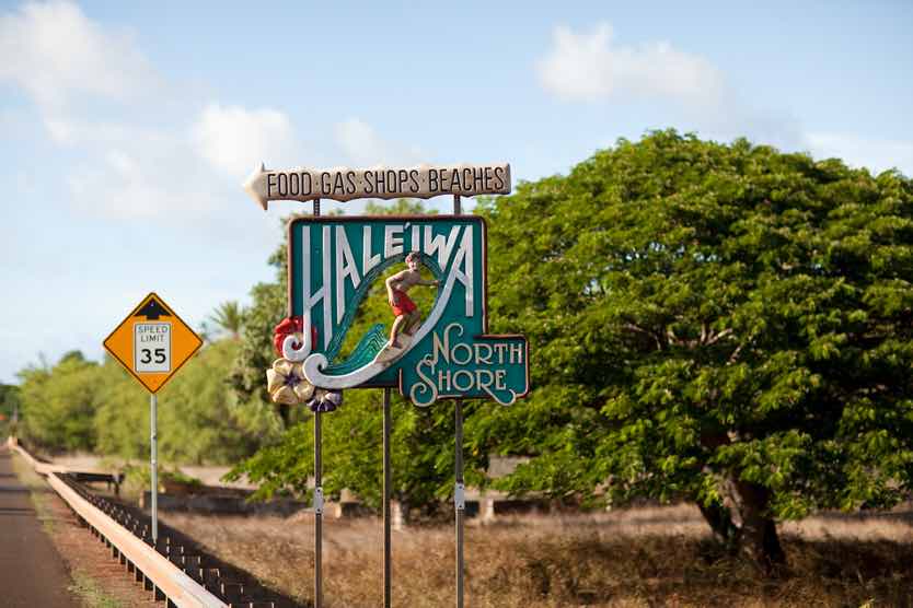 Image of a wooden Haleiwa North Shore sign with a guy surfing a wave and the upper sign says food, gas, shops, beaches with an arrow pointing to the left