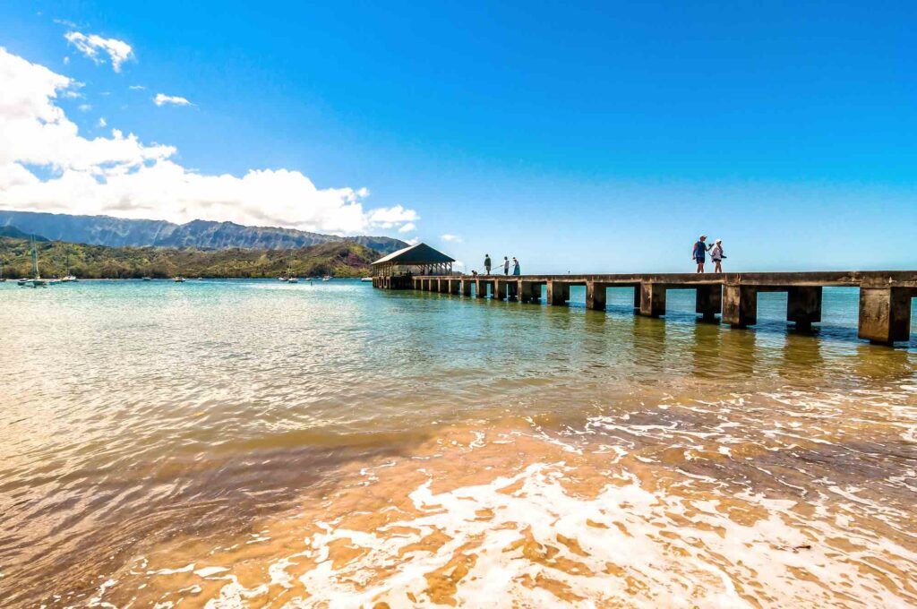 Image of the Hanalei Pier and ocean with green mountains in the background