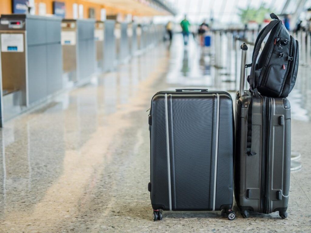 Image of two black rolling carry on bags and a small black backpack at an airport