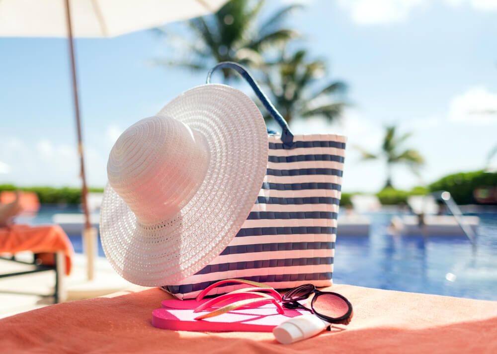 Image of a white sun hat, striped beach bag, sunglasses, and flip flops