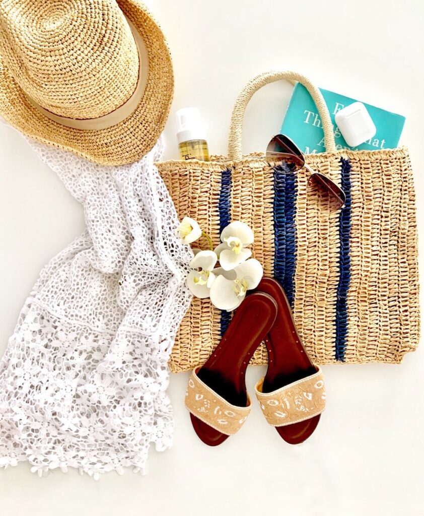 Image of a straw bag with sandals, a white lacy cover up and a straw hat