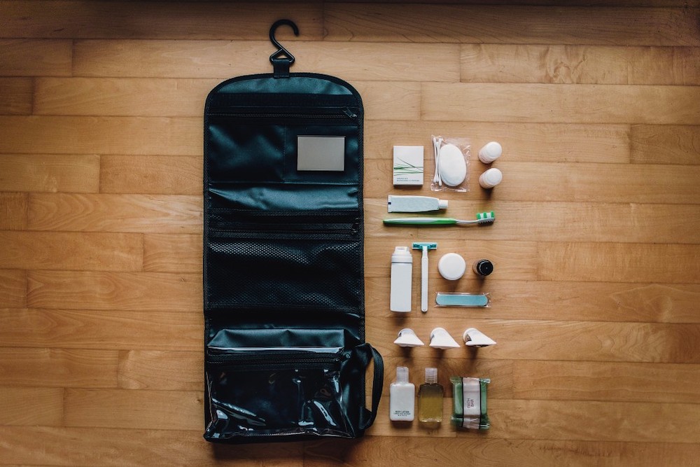 Image of a black hanging toiletry bag with a bunch of toiletries laid out on a wooden background