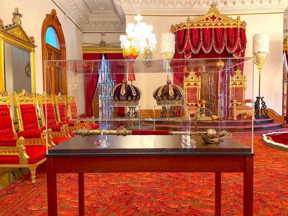 Image of crowns in a glass case with thrones in the background at Iolani Palace in Hawaii