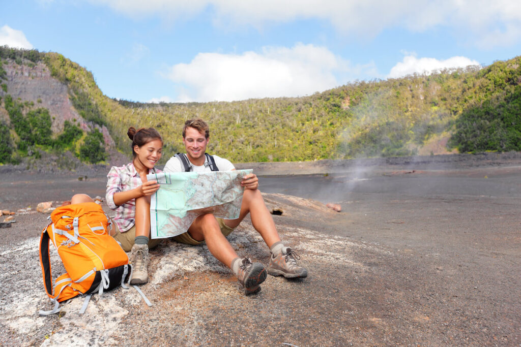 Image of a man and woman hiker reading a map while sitting on the ground at Hawaii Volcanoes National Park.