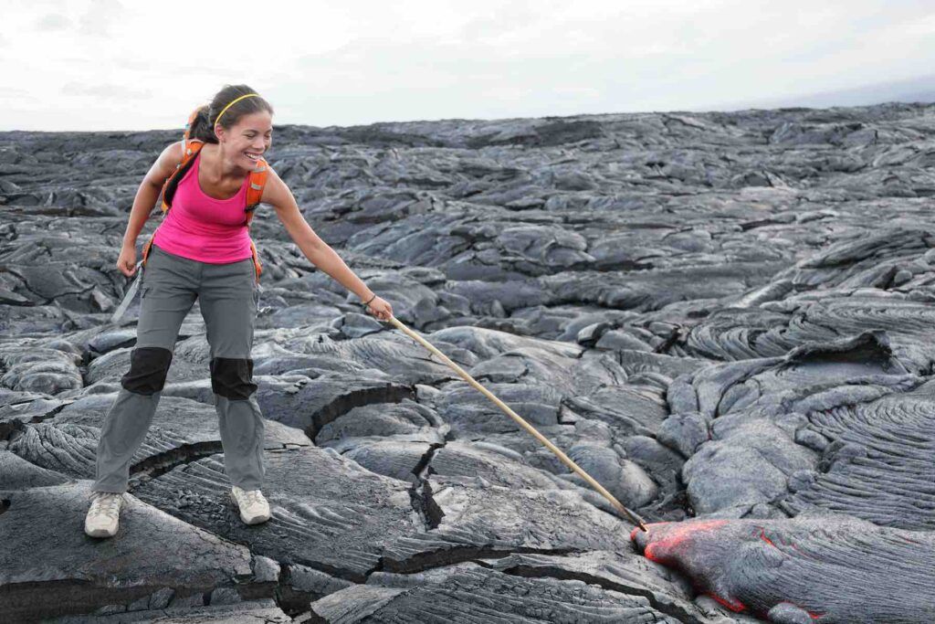 Hawaii Big Island lava tourist on volcano poking stick in red hot moving lava. flowing lava from Kilauea volcano around Hawaii volcanoes national park, USA. Young asian woman hiker.