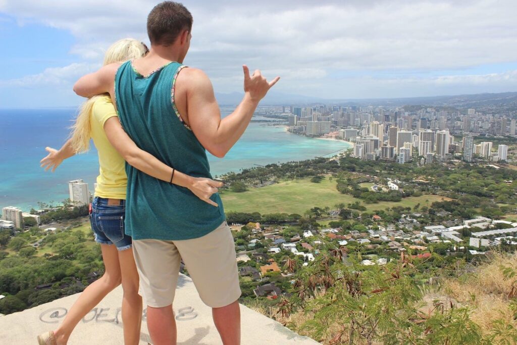 Image of a man and woman throwing shakas while standing at the Diamond Head hike platform overlooking Waikiki