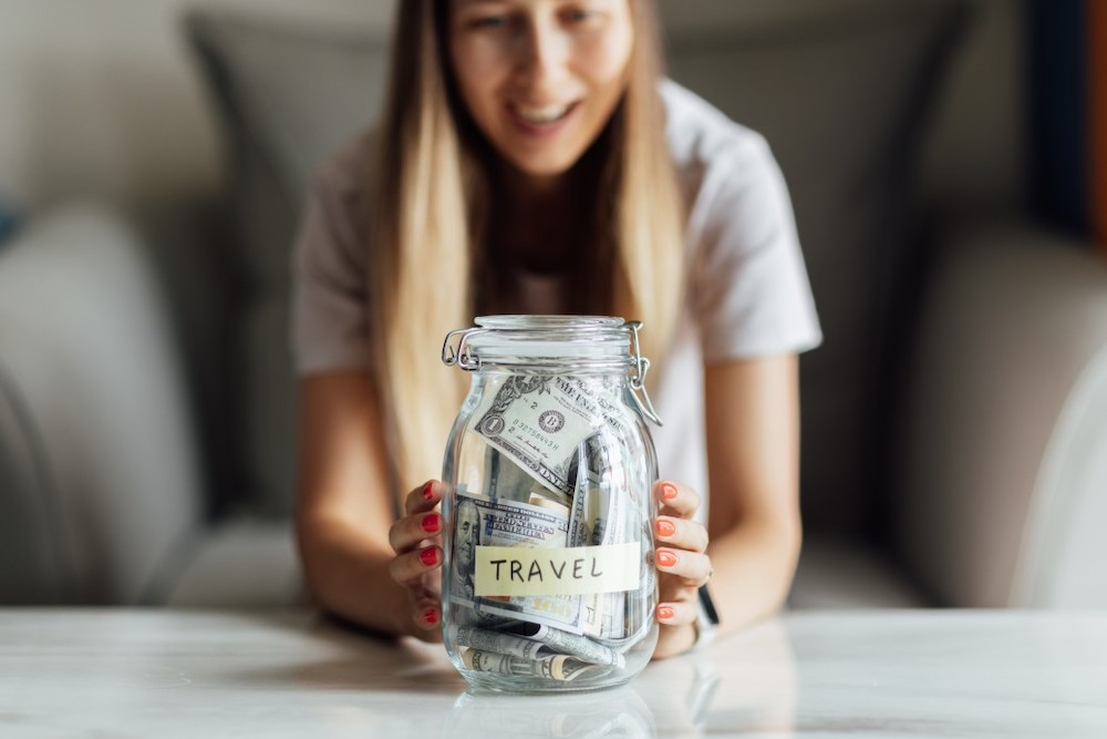 Image of a woman holding a glass jar full of cash with the word travel written on it