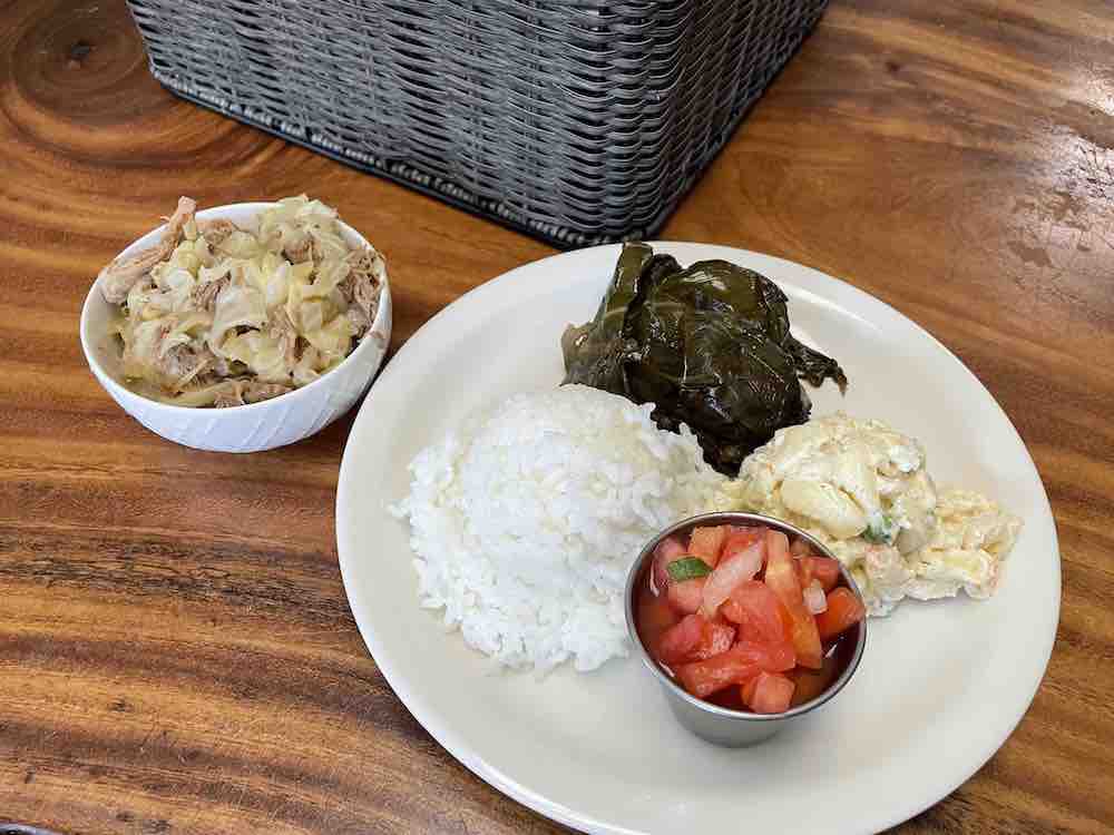 Image of a white plate with chopped up tomatoes, white rice, macaroni salad, and leafy greens