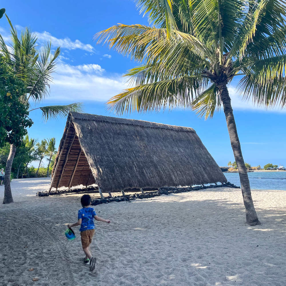 Kaloko-Honokohau National Historic Park and Aiopio Beach on the Big Island. Image of a boy running toward a large fishing hut in Hawaii.