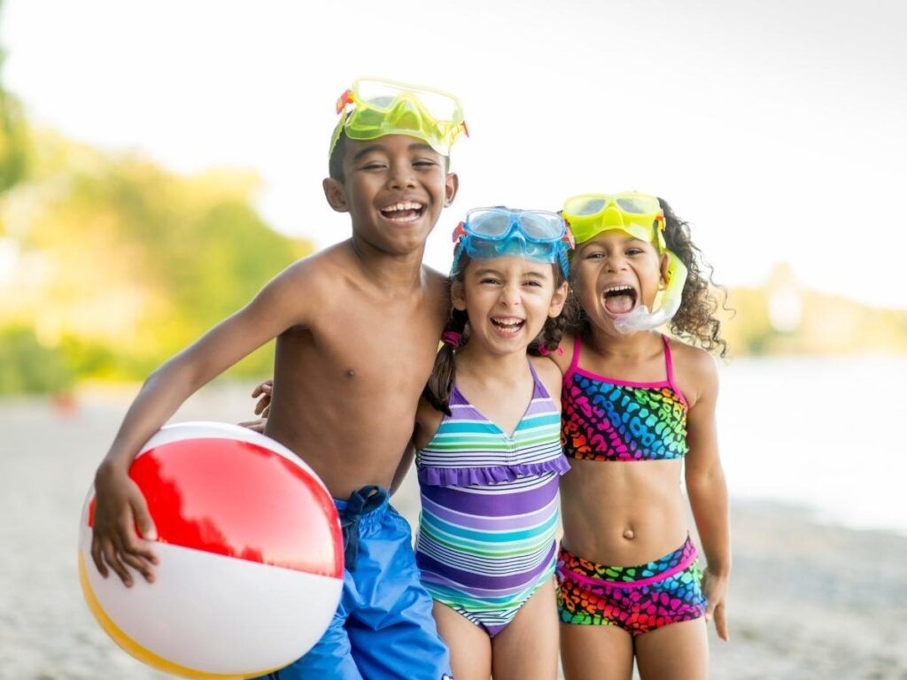 Image of three kids wearing swimsuits  and snorkel masks and holding a beach ball 