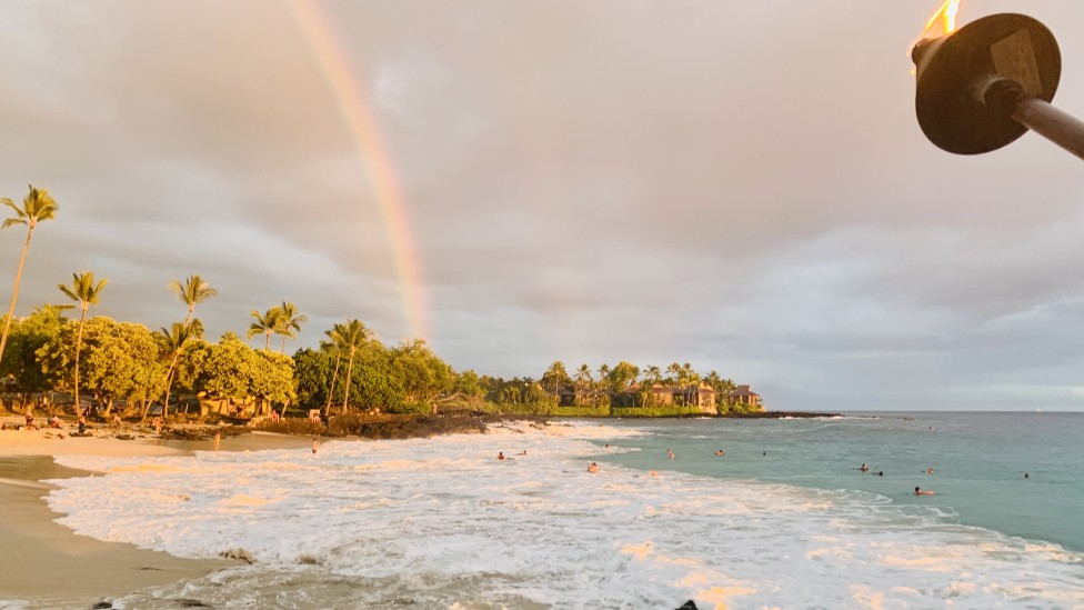 Image of a beach at sunset with a rainbow in the background.