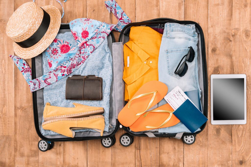 Check out this amazing Maui packing list by top Hawaii blog Hawaii Travel Spot! Image of a suitcase filled th vacation clothing on a hardwood floor