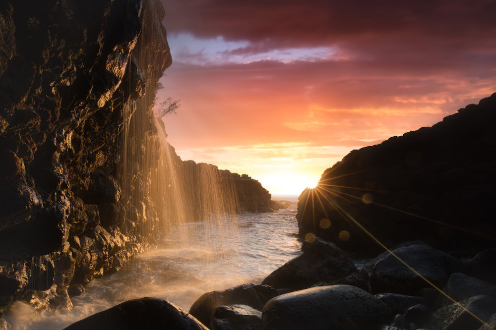 Image of a sunset through giant rocks on North Shore Kauai