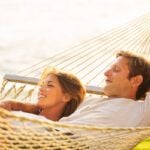 Find out the best Oahu honeymoon resorts recommended by top Hawaii blog Hawaii Travel Spot! Image of a Romantic couple relaxing in tropical hammock at sunset