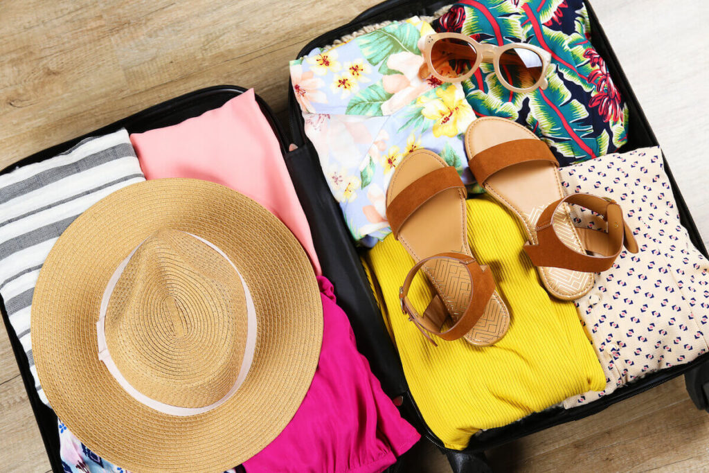 Check out this Oahu packing list by top Hawaii blog Hawaii Travel Spot! Image of a suitscase filled with tropical vacation clothing and a straw hat