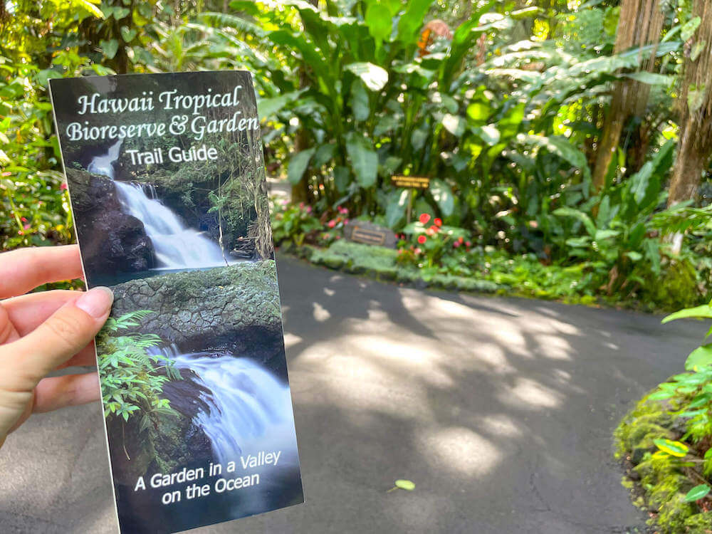 Image of the Hawaii Tropical Bioreserve & Garden trail guide with a lush tropical garden behind it