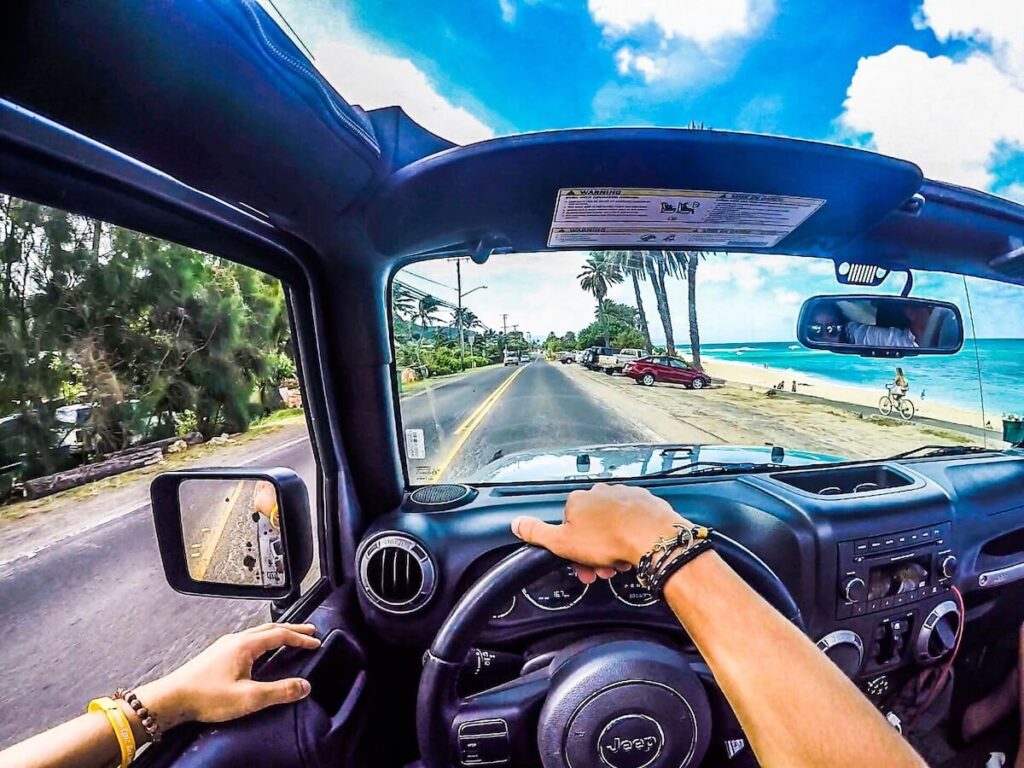 Image of someone driving a Jeep with the top down along a beach road on Oahu