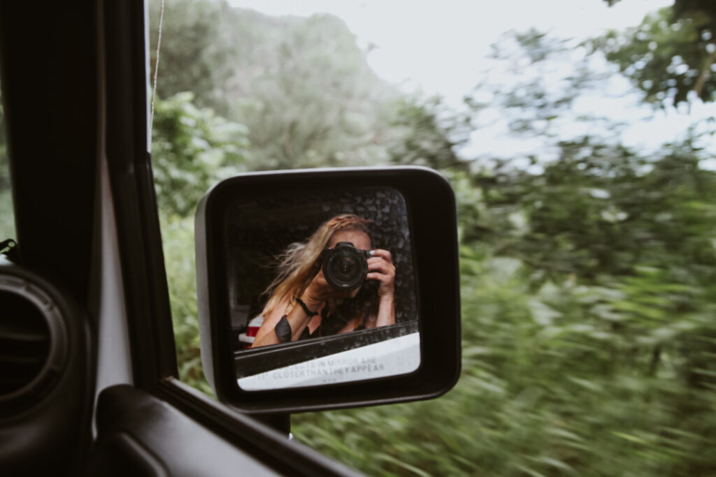 Road to Hana tips: Image of a woman taking a photo out of her car window as a passenger while driving the Road to Hana on Maui