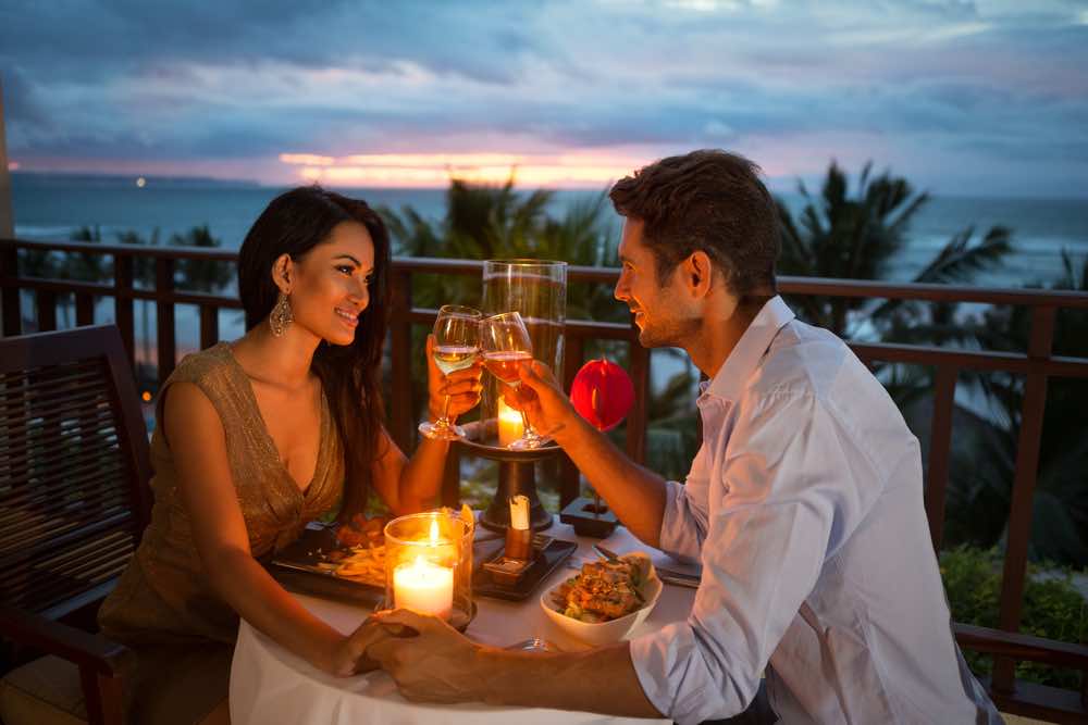 Image of a couple cheering with wine glasses at a candlelight dinner on Maui