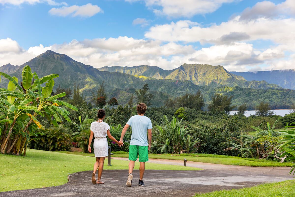 Find out the most romantic Kauai honeymoon resorts recommended by top Hawaii blog Hawaii Travel Spot! Image of a couple holding hands walkind down a path in North Shore Kauai