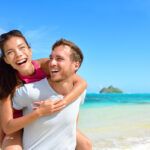 Find out the most romantic things to do in Oahu for couples recommended by top Hawaii blog Hawaii Travel Spot! Image of a man giving a woman a piggy back ride at Lanikai Beach on Oahu