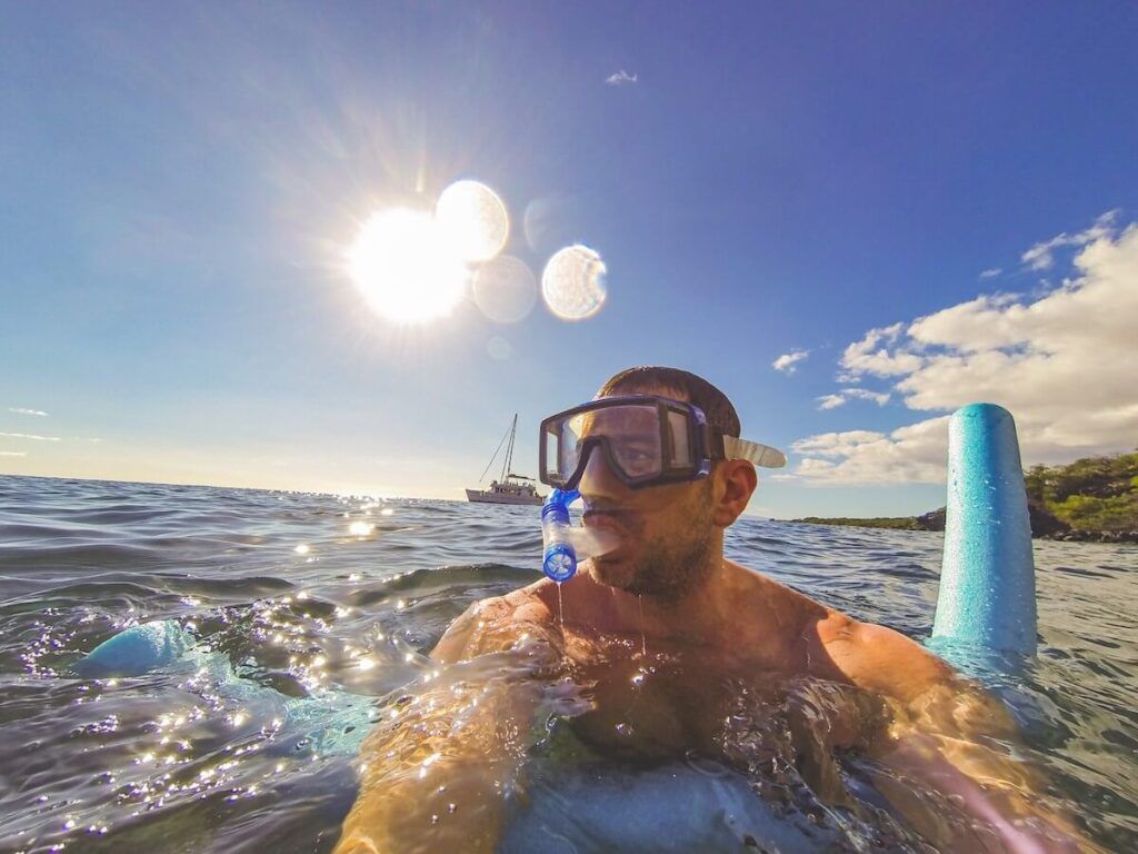 Image of a man holding a pool noodle while snorkeling in Maui with a boat in the background