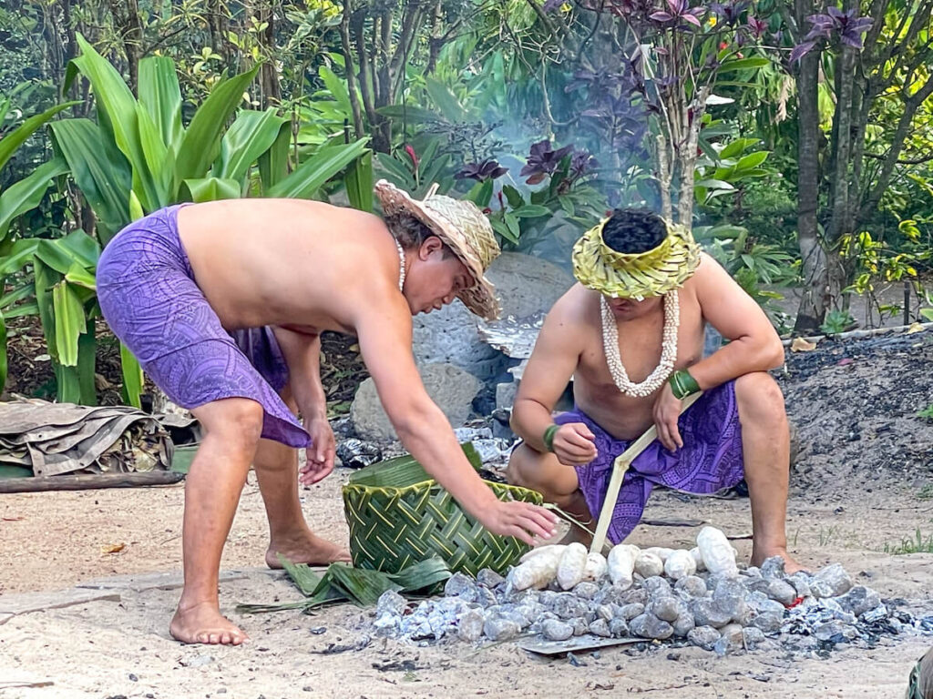 Image of two men wearing purple sarongs while cooking food on an umu at Toa Luau in North Shore Oahu