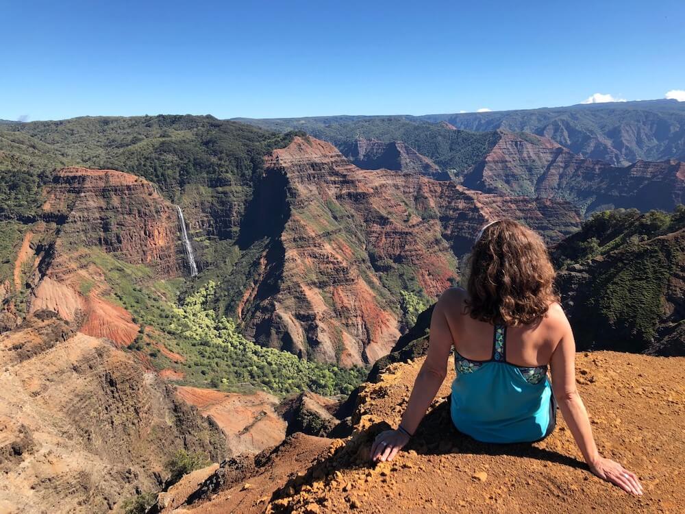 Image of a woman wearing a tank top sitting at the edge of Waimea Canyon on Kauai