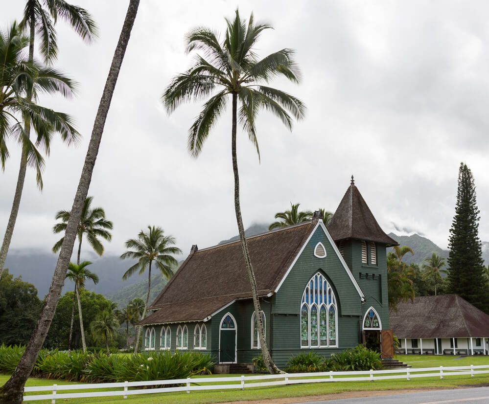 Image of a green church with stained glass windows with palm trees in the background