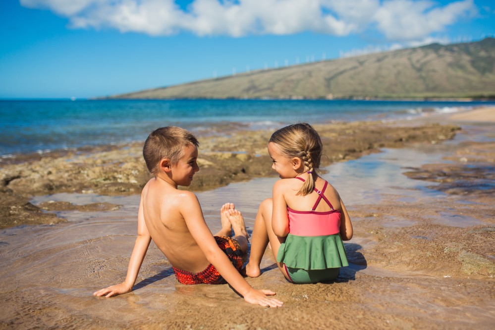 Image of a boy and girl wearing swimsuits sitting a beach in Hawaii