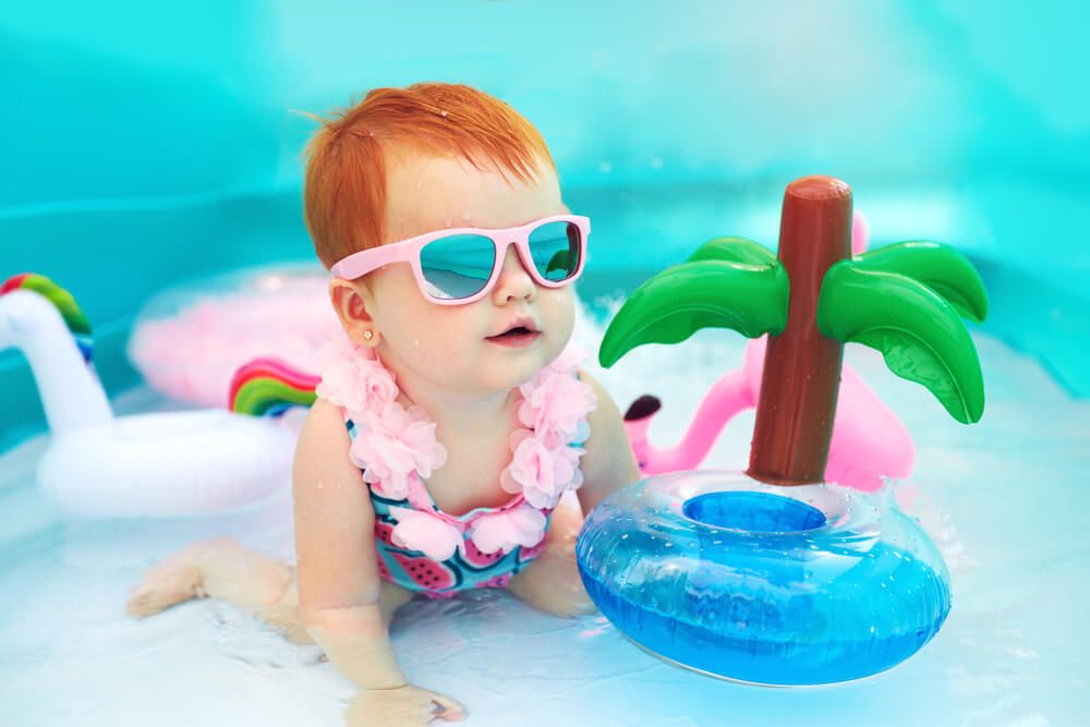 Image of a red-headed baby in a kiddie pool with an inflatable palm tree