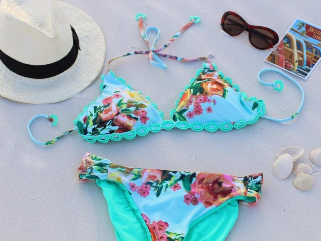 Image of a blue floral bikini, sunglasses, a straw fedora, and a postcard