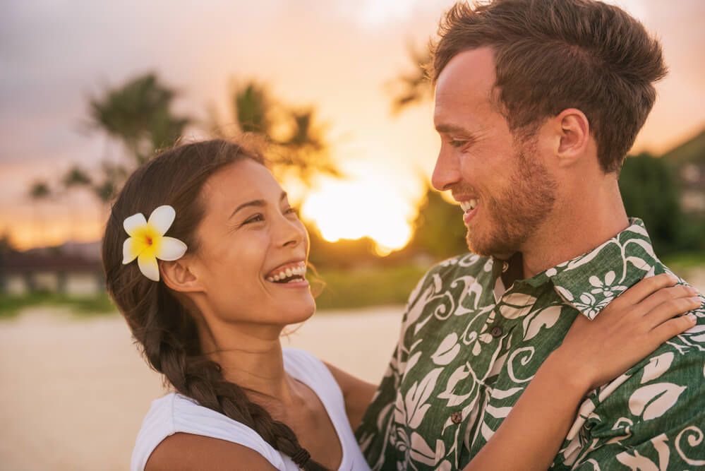 Image of a woman with a flower behind her ear laughing with a man wearing a green aloha shirt in Hawaii