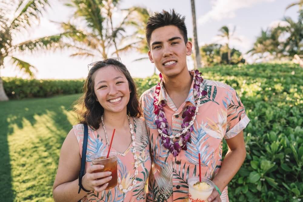 Image of a man and woman wearing matching pink Aloha shirts while holding tropical drinks at a luau in Hawaii