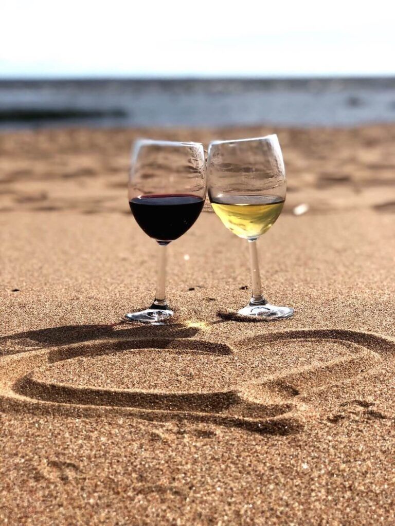 Image of two wine glasses on a beach with a heart drawn into the sand