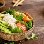 Find out the best Big Island cheap eats recommended by top Hawaii blog Hawaii Travel Spot! Image of Hawaiian poke coconut bowl with grilled salmon fish, rice and avocado. Healthy food