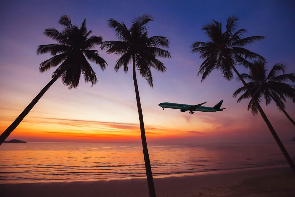 Try to book a direct flight to Hawaii Big Island. Image of an airplane flying over a beach at sunset