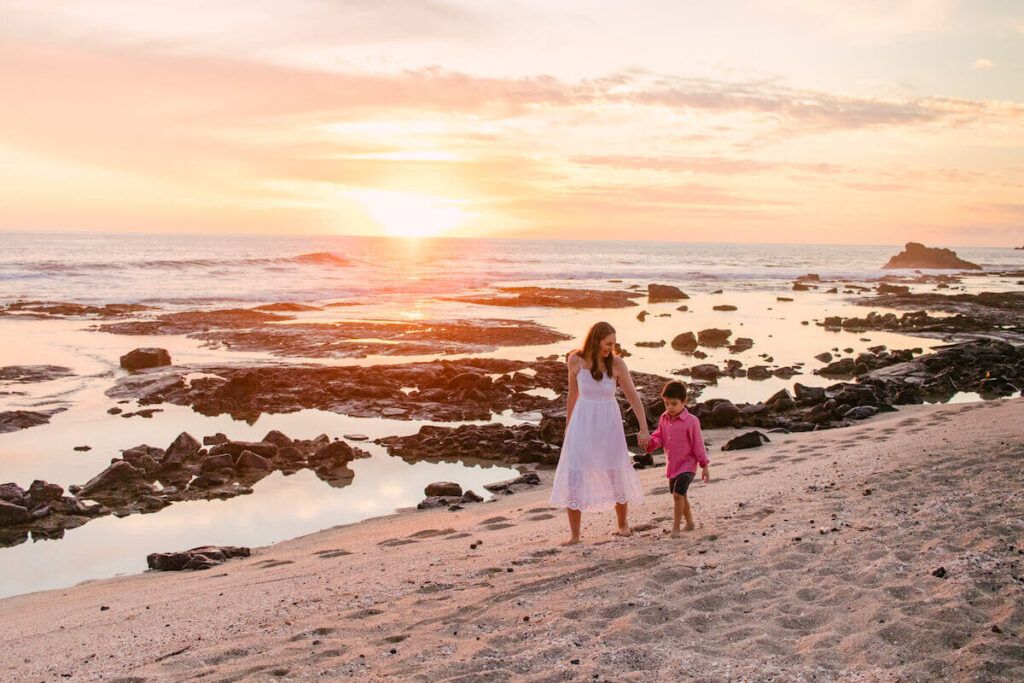 Old Kona Airport State Park. Image of a mom and son holding hands while walking on a beach at sunset.