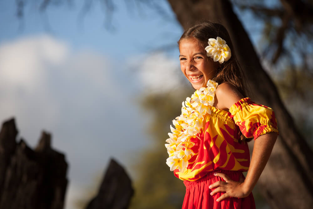 Image of a girl hula dancer wearing a flower in her hair and a plumeria lei and hula clothing