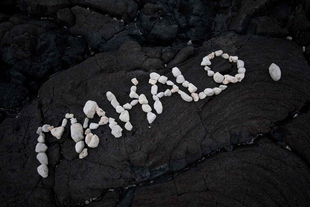 Image of the word Mahalo written in white stones on top of lava rock in Hawaii