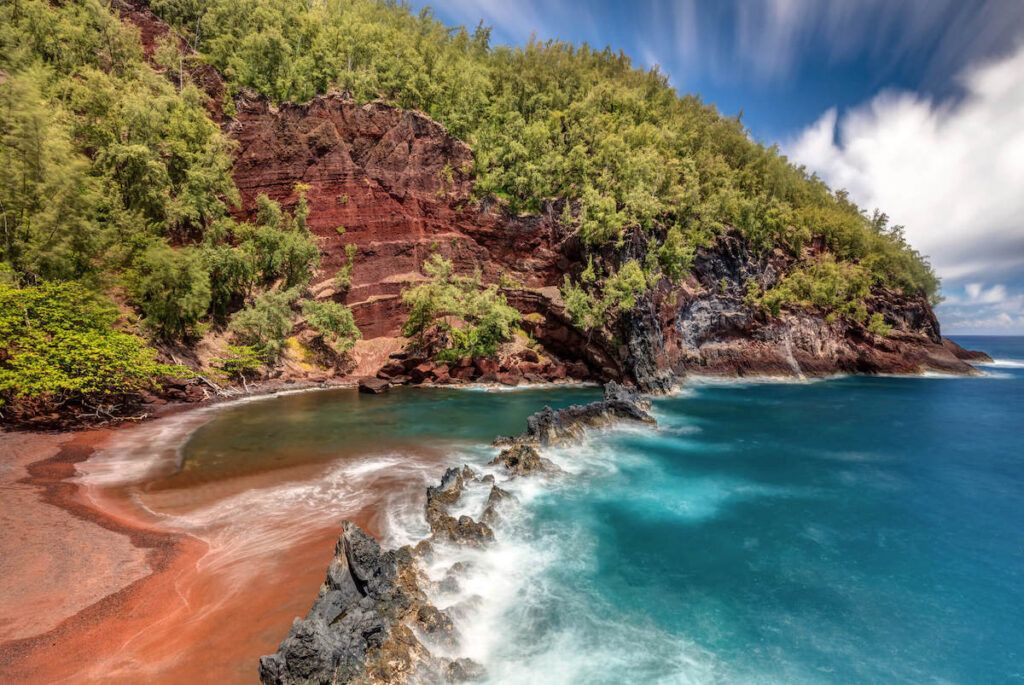 Kaihalulu Beach in Hana Maui. Image of a red sand beach with trees in the background