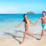 Find out how to plan an affordable Hawaii honeymoon on a budget by top Hawaii blog Hawaii Travel Spot! Image of a couple holding hands while running down a beach on Oahu